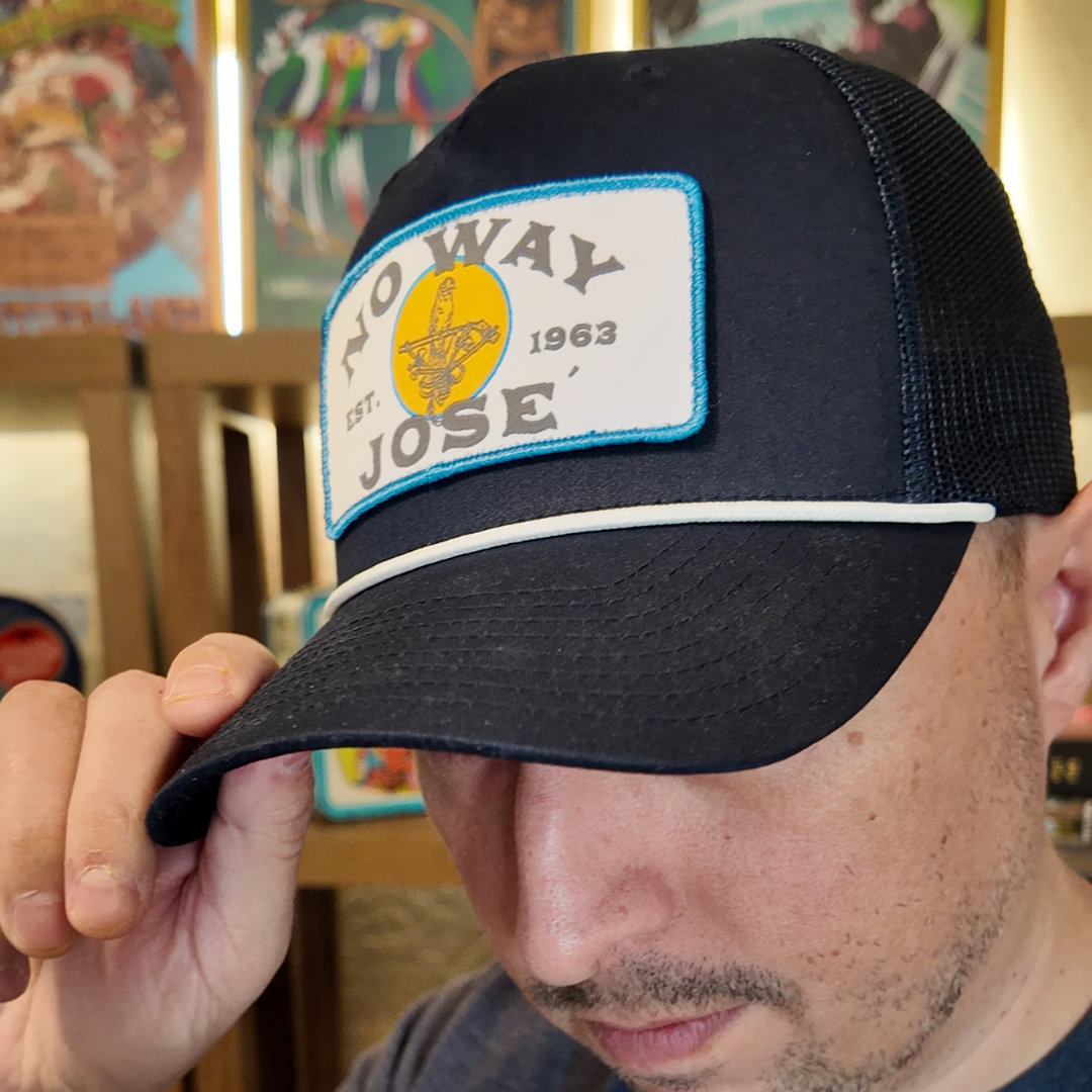 Person wearing a black cap with a 'No Way Jose' patch in an indoor setting.