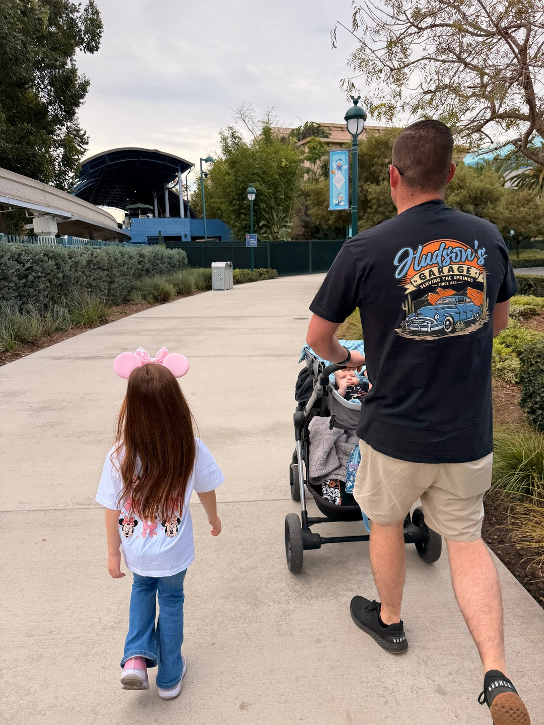 A dad in his Hudson's Garage tee walking with his daughter at the park