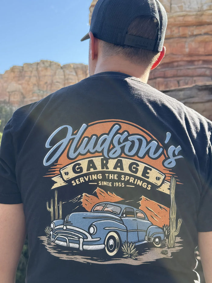 Man wearing a navy Hudson's Garage Corner of Main tee, back view at Disneyland