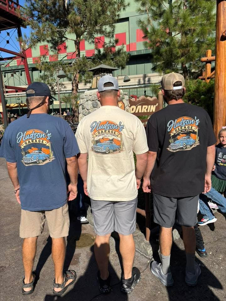 Three men from behind wearing Hudson's Garage Corner of Main tees at the park