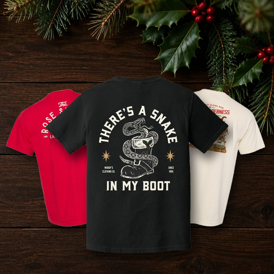 Christmas Snake in My Boot, Rose Suchak Ladder Co and Big Thunder Christmas tees on dark wood with evergreen and holly